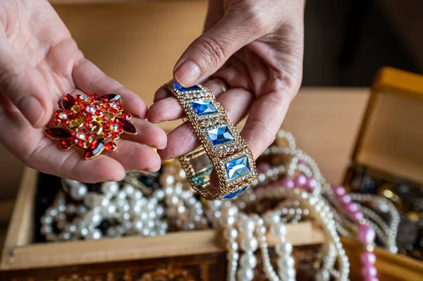 Wooden treasure chest with valuables. A woman holds beads, necklaces and other jewelry in her hands.