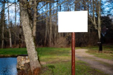 Empty information board on a wooden pole on the forest. Mock-up, attention sign, warning board