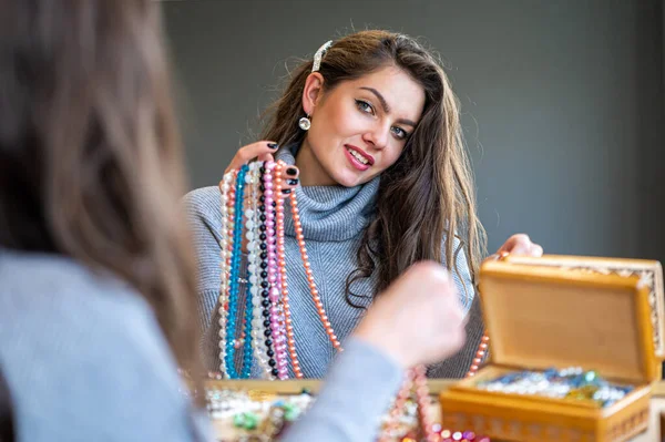 reflection of a woman in mirror choosing and trying different jewelry, soft focus, close-up