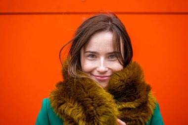 Modern bir ofis binasının turuncu duvarının yanında zarif giyimli bir iş kadınının portresi.