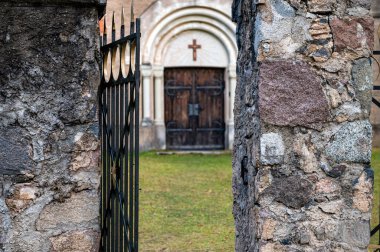 A fragment of a church fence with an open iron gate in the background of the church entrance