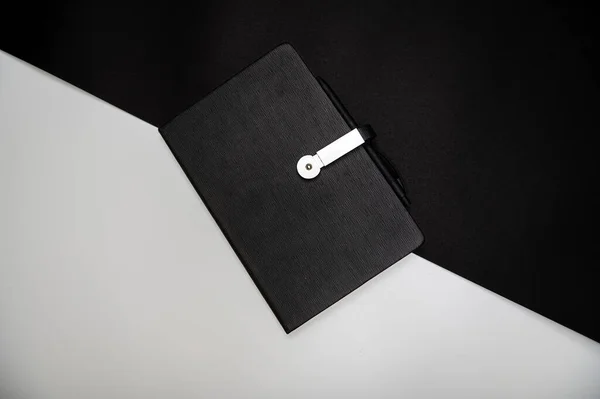 black planner or notebook with pen on two-color black and white background, mockup, copy space
