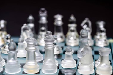 clear glass, transparent chess pieces on a checkerboard, selective focus, closeup, isolated on black