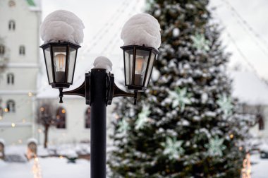 Karlı fener süslemeli Noel ağacı ve bulanık arka planda kilise, sığ alan derinliği