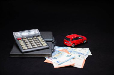 euro banknotes, calculator, notebook and red toy car on black background, loan and insurance concept