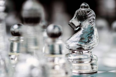 transparent glass chess on dark background, selective focus on knight piece, close-up