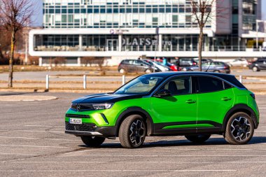 Riga, Letonya - 26 Mart 2021: yeşil elektrikli araç Opel Mokka-e kentsel yerleşim alanının arka planındaki otoparkta