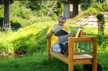 Mature man with laptop and documents working outside in garden, green home office concept.