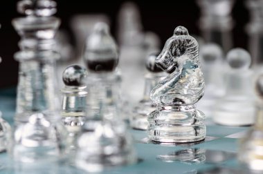 transparent glass chess on dark background, selective focus on knight piece, close-up