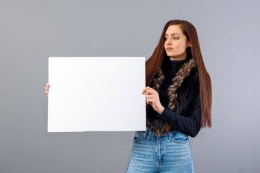 Zarif genç bir bayan, gri üzerinde izole edilmiş, fotokopi alanı ile boş tabela gösteriyor.