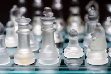 clear glass, transparent chess pieces on a checkerboard, selective focus, closeup, isolated on black
