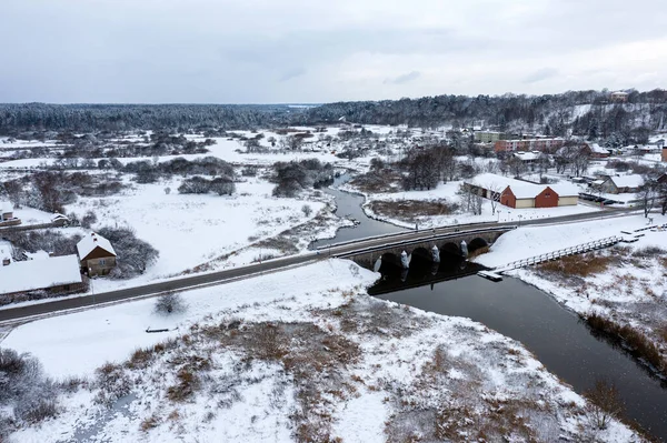 Karlı bir kış gününde Abava nehri üzerinde kemerleri olan eski bir taş köprü, Kandava, hava manzaralı.