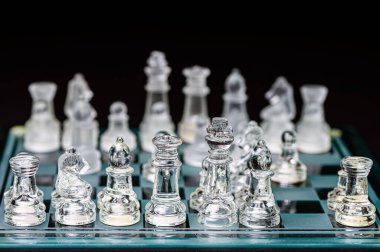 clear glass, transparent chess pieces on a checkerboard, selective focus, closeup, isolated on black