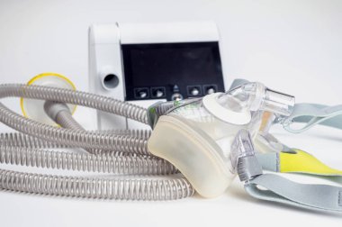 Beyaz zemin üzerinde CPAP makinesi, maske ve tüp içeren sürekli pozitif hava yolu basınç sistemi.