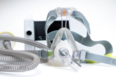 Beyaz zemin üzerinde CPAP makinesi, maske ve tüp içeren sürekli pozitif hava yolu basınç sistemi.