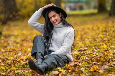 Güz parkında beyaz kazaklı ve siyah şapkalı güzel esmer kadın.