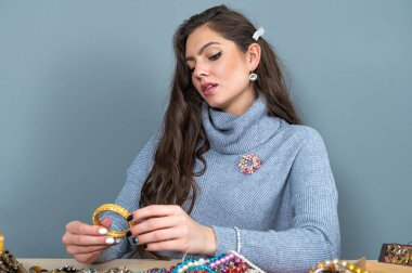 Masada bir sürü mücevherle oturan ince esmer, farklı mücevherler seçiyor ve deniyor.