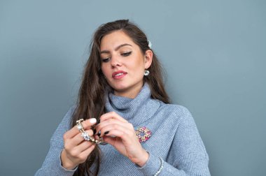 Uzun gri kazaklı zarif, ince kadın mücevherlere bakıyor, arka planda izole edilmiş, kopyalama alanı var.