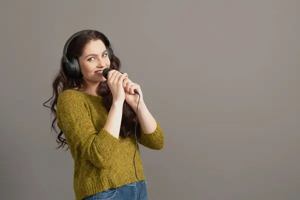 expressive teenager female singing with a microphone and headphones, isolated on gray