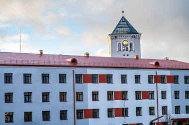 Günbatımı gökyüzünün arka planında bir saat ve modern bir binanın bir parçası olan beyaz bir kule..