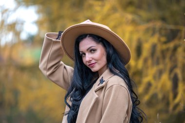 Açık havada bej ceketli ve şapkalı güzel bir esmer kadının portresi.