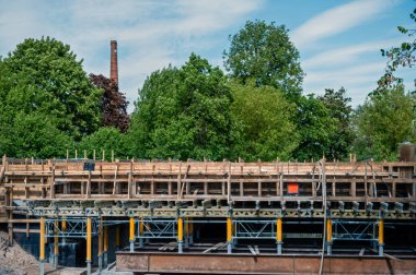 Yeşil ağaçların ve mavi gökyüzünün arka planında iskelesi olan inşaat alanı