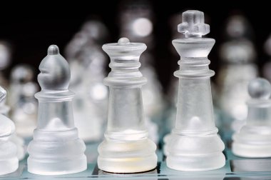 clear glass, transparent chess pieces on a checkerboard, selective focus, closeup, isolated on black