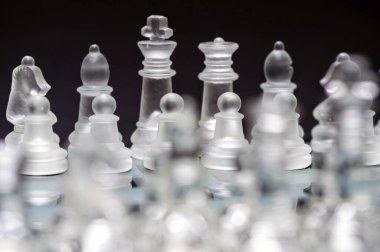 clear glass, transparent chess pieces on a checkerboard, selective focus, closeup, isolated on black