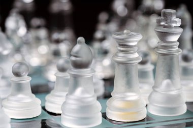 clear glass, transparent chess pieces on a checkerboard, selective focus, closeup, isolated on black