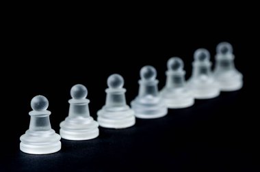opaque glass chess pawn row on black background, selective focus, close-up