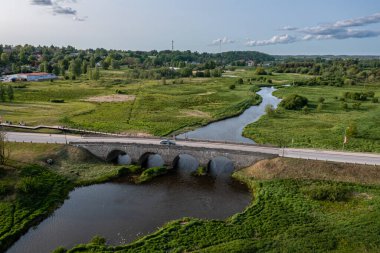 Çimenli alanda nehir boyunca uzanan taş köprü. Kandava, Letonya
