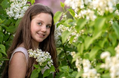 Genç bir kız çiçek açan leylak çalılığında duruyor. Seçici odak ve kopyalama alanı olan arkaplan