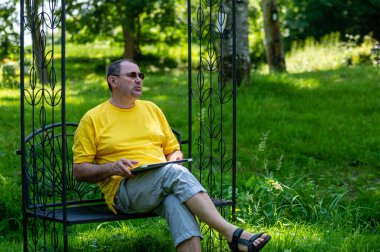 middle aged man with laptop working outside in garden, green home office concept