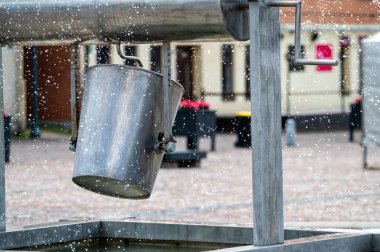 Kasabadaki bir çeşmede metal bir kova asılı duruyor. Seçici odak ve kopyalama alanı olan arkaplan