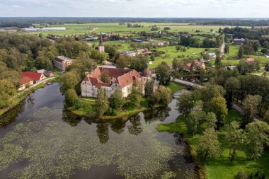 Etrafı su, ağaçlar ve yeşil tarlalarla çevrili bir ortaçağ kalesi. Sarılık, Letonya