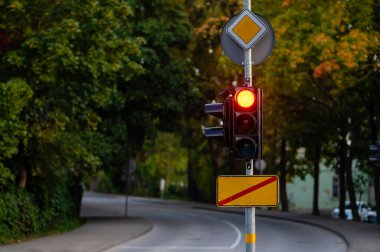 Sonbahar şehrinin odaksız arka planında kırmızı ışığı olan trafik semaforu, yakın plan