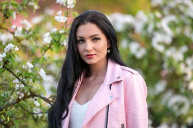 Pembe ceketli bir kadın çiçek açan bir ağacın yanında gülümsüyor. Suyun sığ derinliği