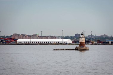 New York, ABD - 7 Haziran 2019: Tarihi bir deniz feneri arka planda kargo faaliyetlerinin olduğu sakin bir limana bakıyor.