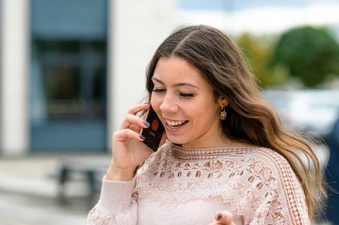 Neşeli genç bir kadın dışarıda canlı bir telefon görüşmesi yapıyor..
