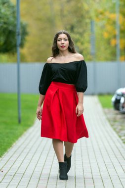 Bir kadın sonbahar yaprakları arasında şık bir kıyafet giyerek yolda yürüyor..