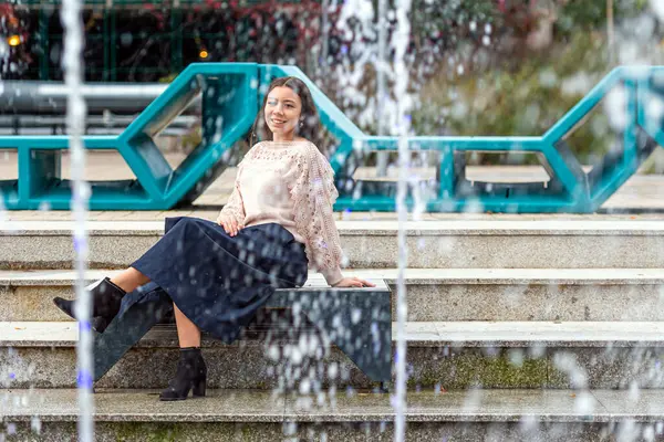 stock image A young woman enjoys a peaceful moment beside a stunning fountain.