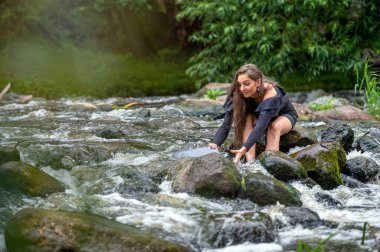 a woman uses a computer while sitting on a rock in the river,laptop falls into water, accident