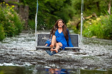 a smiling young woman swings on a rope swing across a fast-flowing river