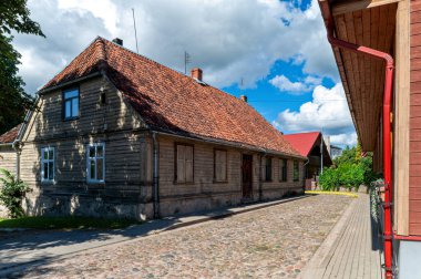 Tukums, Letonya - 22 Ağustos 2024 Güneşli bir günde ahşap bir ev kaldırım taşı yolunun yanında duruyor.