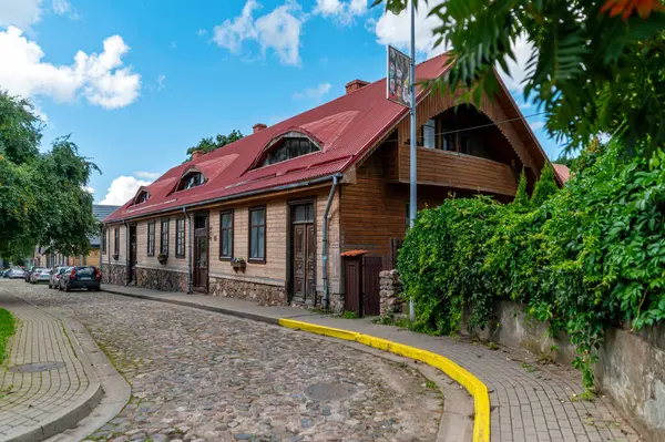 stock image Tukums, Latvia - August 22, 2024: A cozy wooden house with a red roof along a winding cobblestone street.