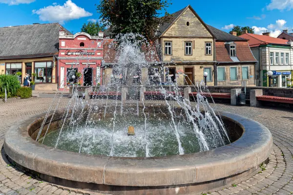 stock image Tukums, Latvia - August 22, 2024: A lively fountain sprays water in a picturesque town square filled with shops.