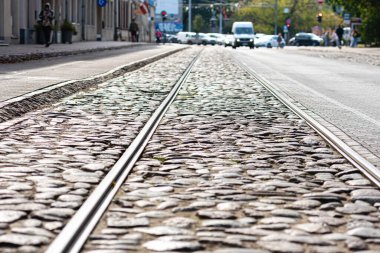 Tramvay izleri güneş ışığında parlayan bir kaldırım taşı caddesi boyunca ilerliyor..