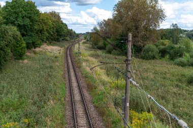 A train track winds through vibrant green fields under a blue sky. clipart