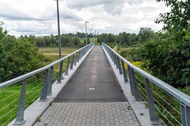 Geniş bir yaya köprüsü bulutlu bir gökyüzünün altında canlı yeşil üzerine uzanır..