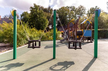 Parlak ve güneşli bir oyun parkında salıncaklar boş duruyor..